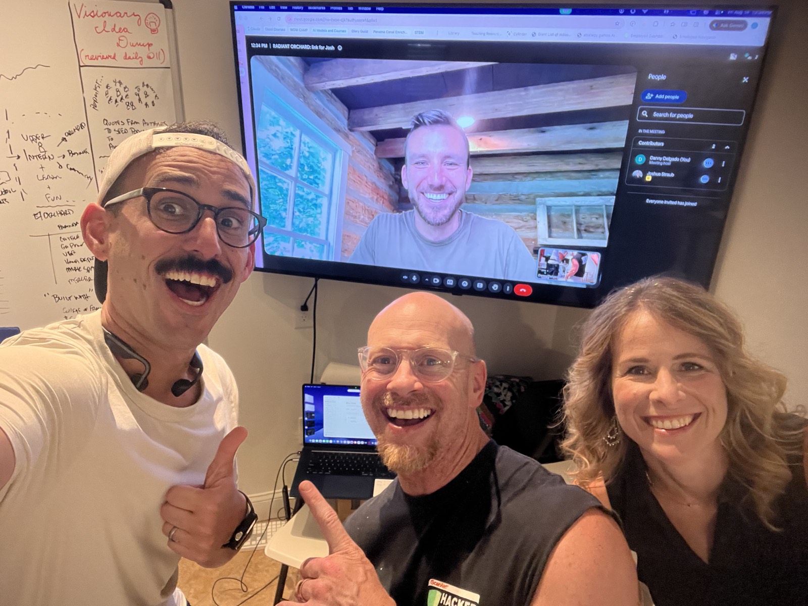Kevin, Danny, and Sarah gathered at the working table, with Josh joining by video call on the screen behind them and a whiteboard of ideas alongside.