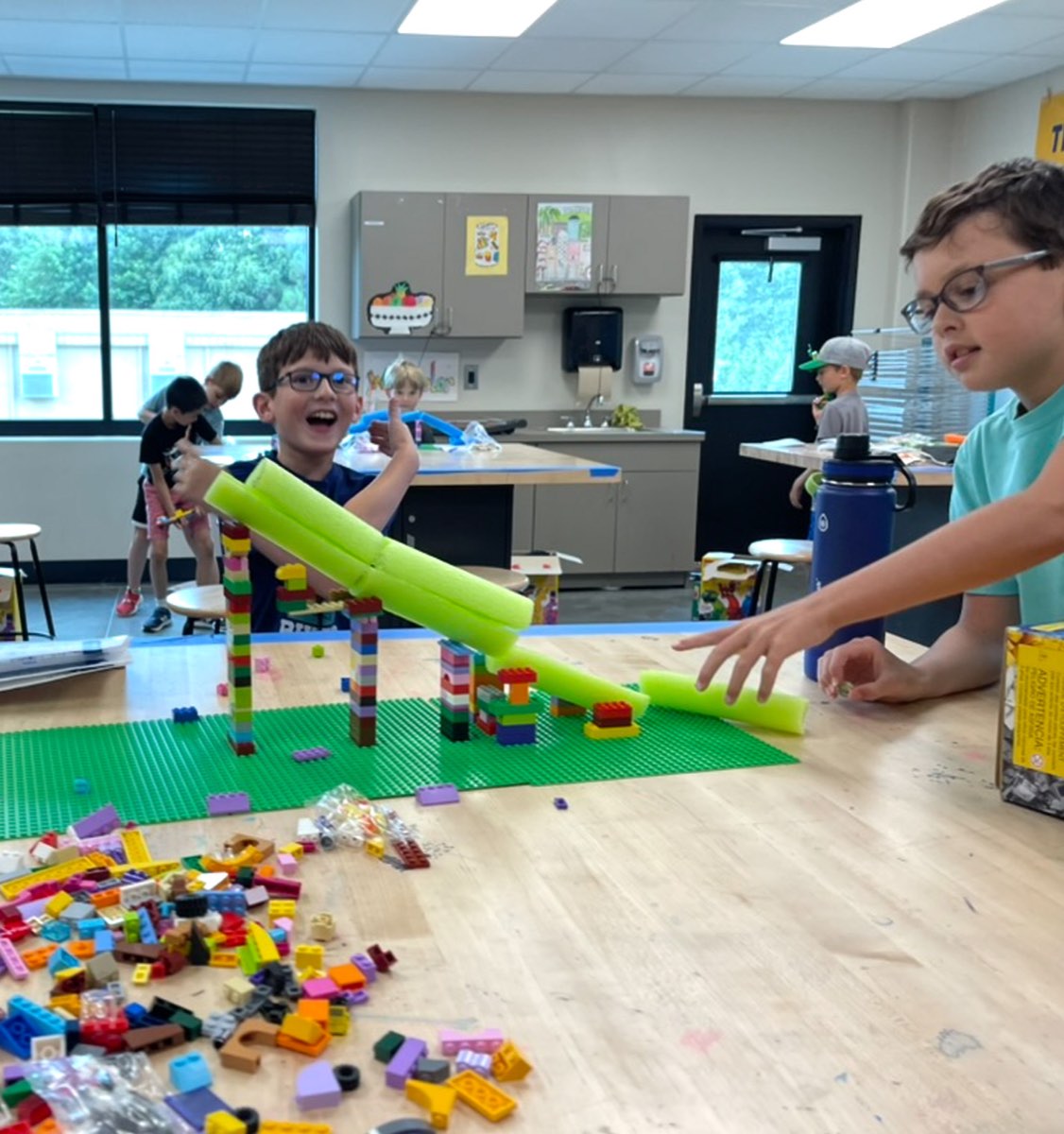 Kids at WOW Camp building a marble run from colorful blocks and pool-noodle ramps, one grinning with a thumbs up.